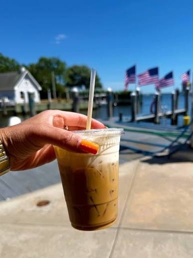 An iced coffee held up on the Low Tide dock, with American flags and the canal behind it